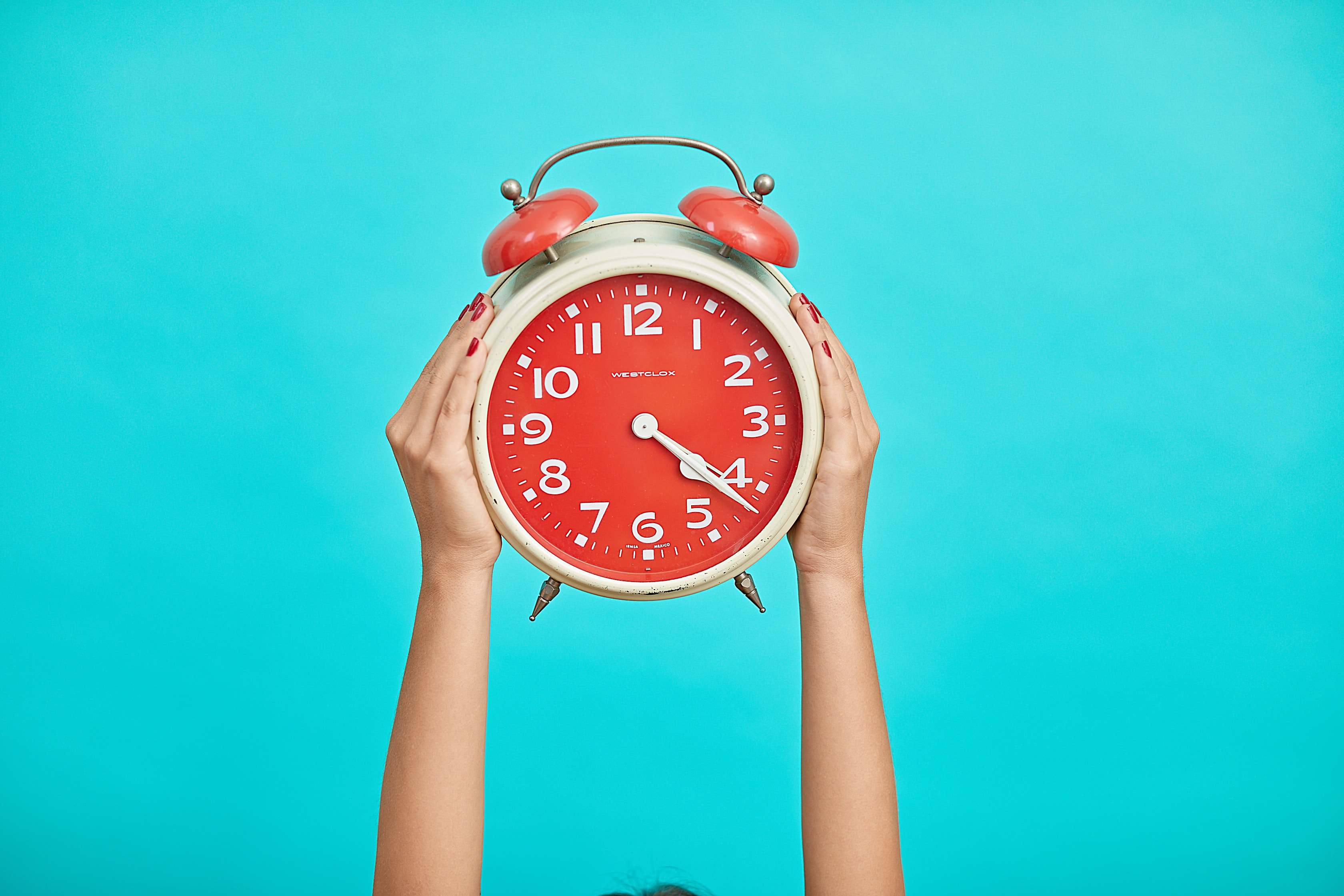 Person holding red alarm clock on blue background